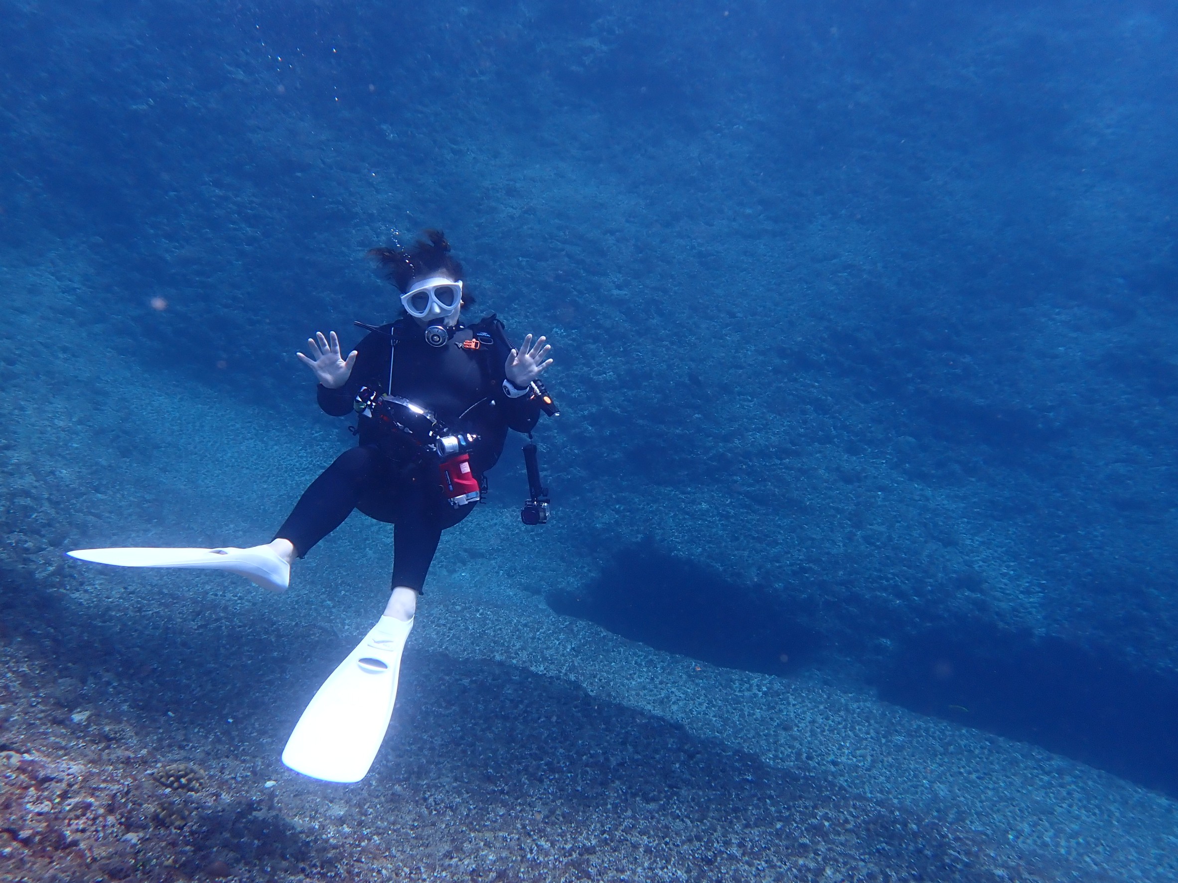 真っ青な海で女性ダイバーが体育座りの格好でこちらを向いて浮いている。両手は楽しそうにパーと広げている。